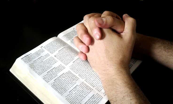 A person is praying using the Bible